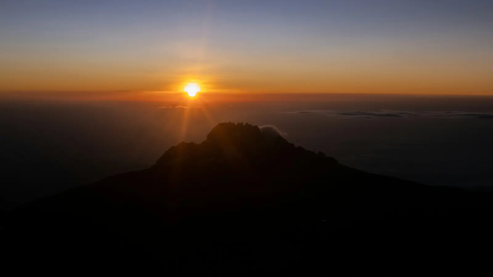 The sun rising over a dark mountain summit above a sea of clouds
